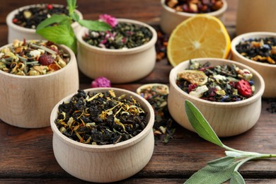 Photo of Different kinds of dry herbal tea in bowls on wooden table