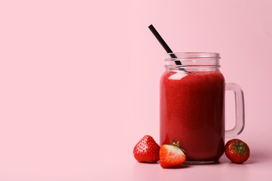 Photo of Mason jar with delicious berry smoothie and fresh strawberries on pink background. Space for text