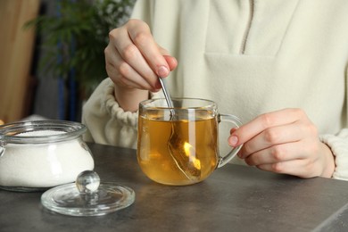 Woman stirring sugar in tea at grey table, closeup