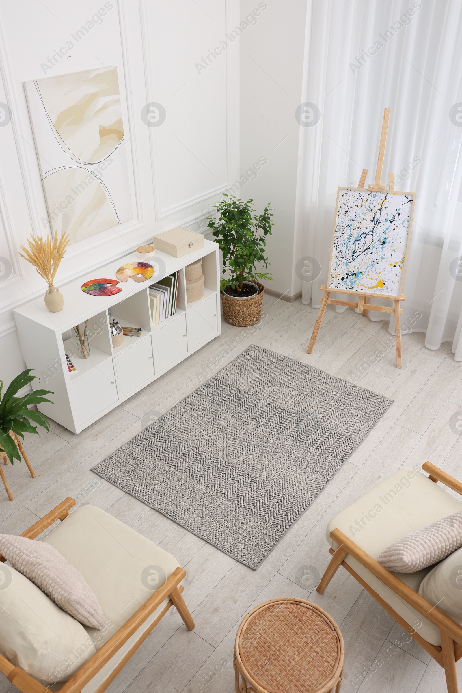 Photo of Stylish room with beautiful rug, easel and furniture, above view. Interior design