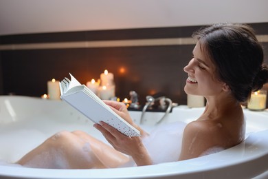 Photo of Young woman reading book while taking bubble bath. Romantic atmosphere