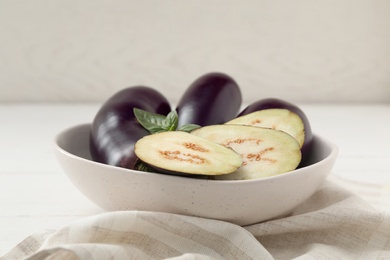 Photo of Cut and whole purple eggplants with basil on table, closeup