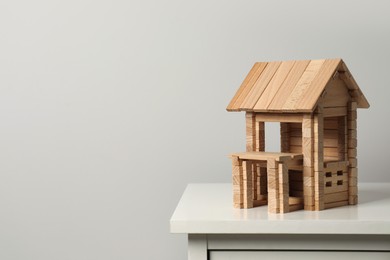 Photo of Wooden house on chest of drawers near light grey wall, space for text. Children's toy