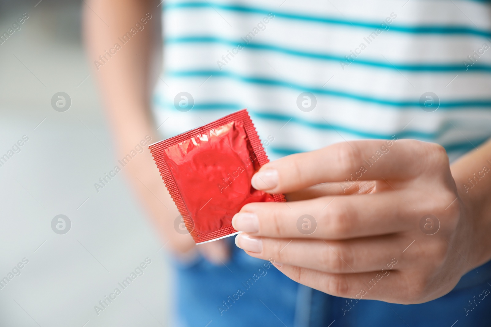 Photo of Woman holding condom indoors, closeup. Safe sex concept