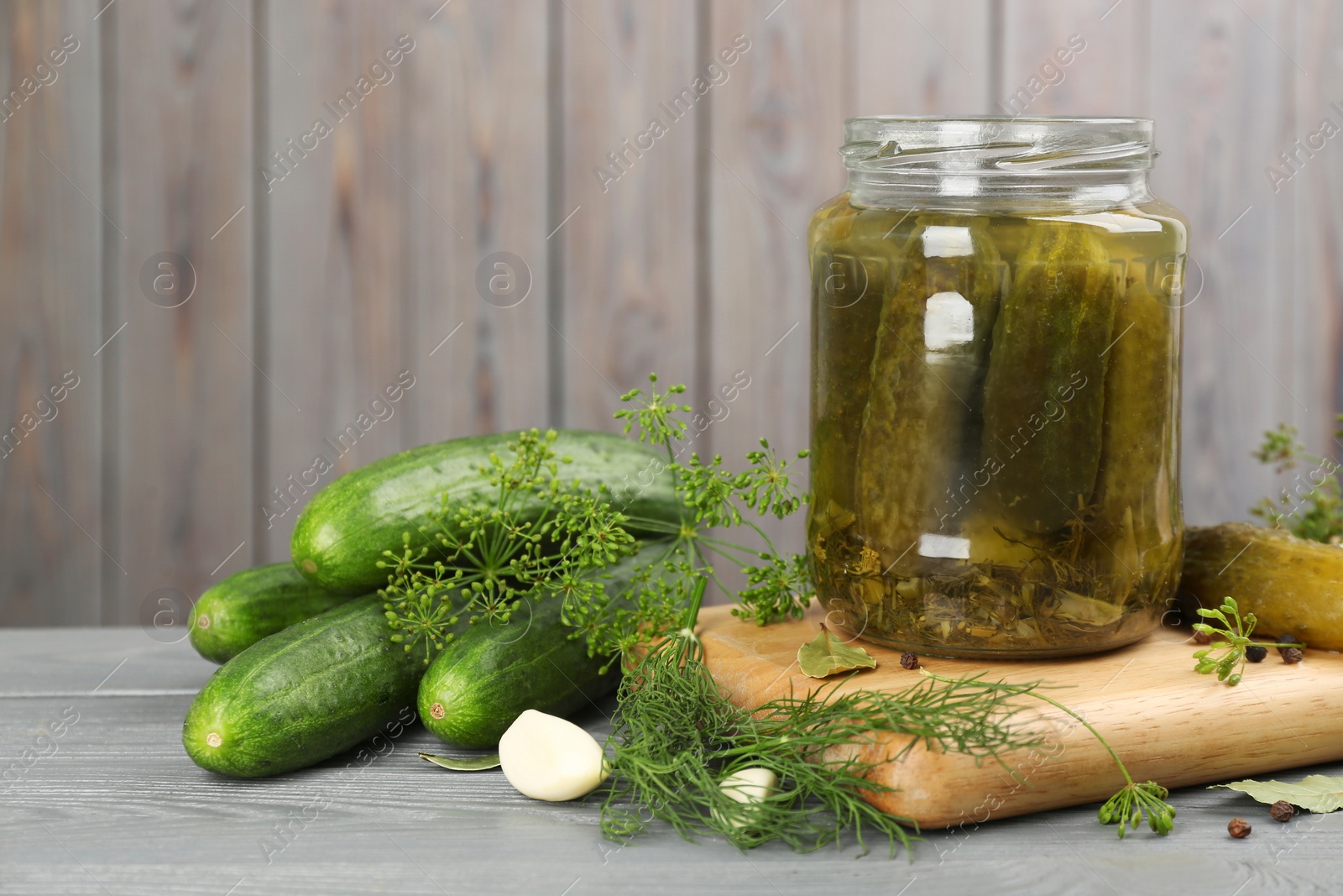 Photo of Glass jar of pickled cucumbers and ingredients on grey wooden table