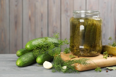 Glass jar of pickled cucumbers and ingredients on grey wooden table