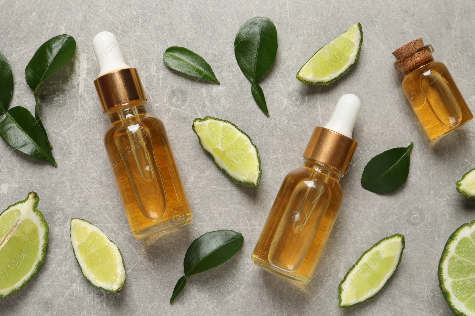 Photo of Glass bottles of bergamot essential oil and fresh fruits on light grey table, flat lay