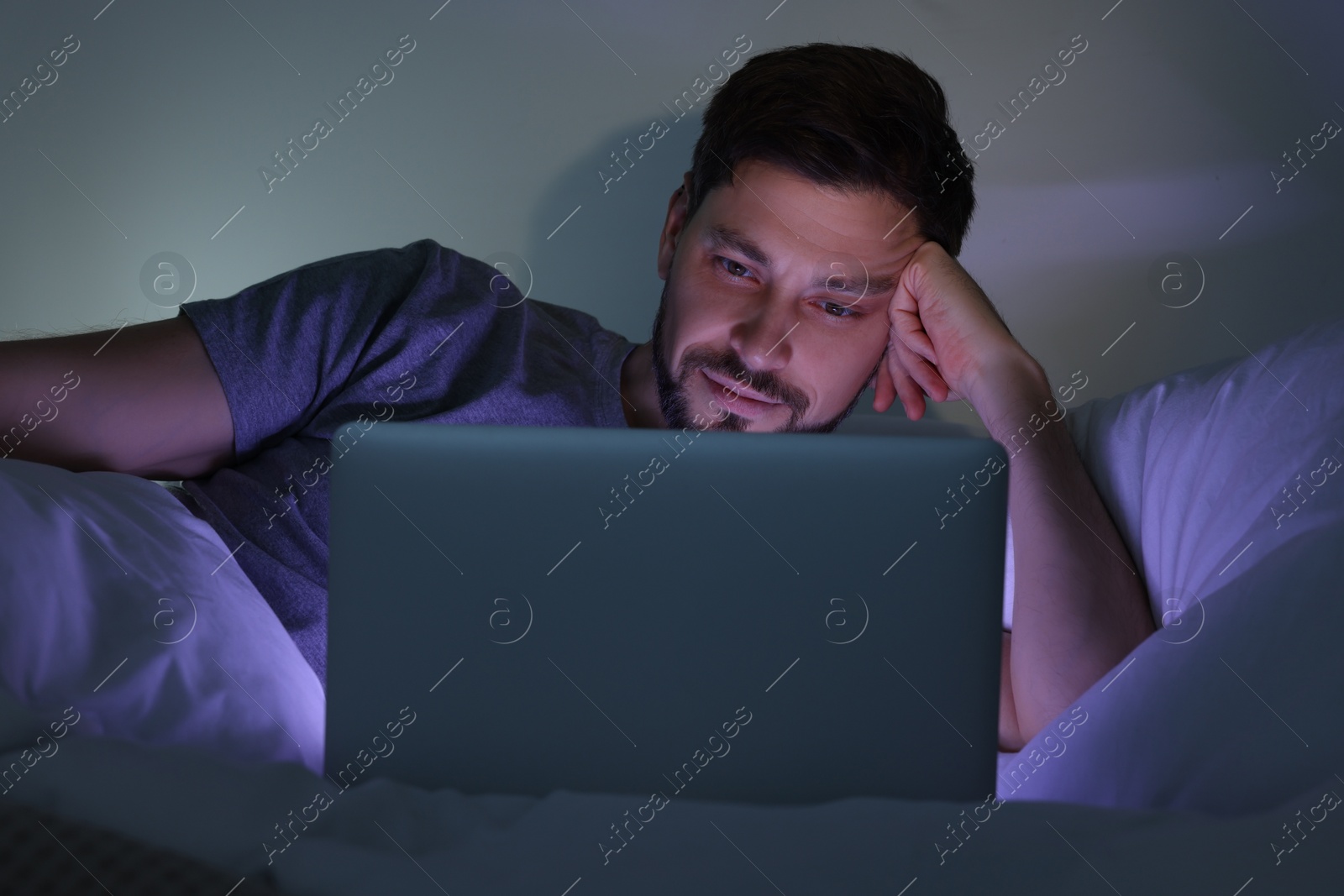 Photo of Man using laptop in bed at night. Internet addiction