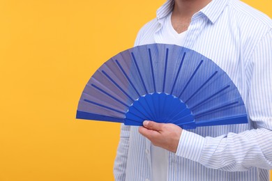 Man holding hand fan on orange background, closeup. Space for text