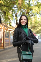 Photo of Beautiful young woman with leather gloves and stylish green bag on city street