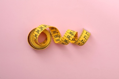 Yellow measuring tape on pink background, top view