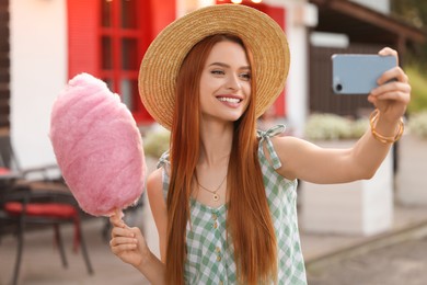 Photo of Smiling woman with cotton candy taking selfie outdoors