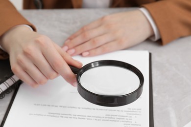 Woman looking at document through magnifier at light gray table, closeup. Searching concept