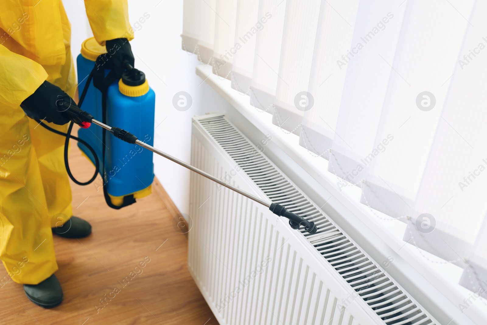 Photo of Pest control worker in protective suit spraying pesticide indoors, closeup. Space for text