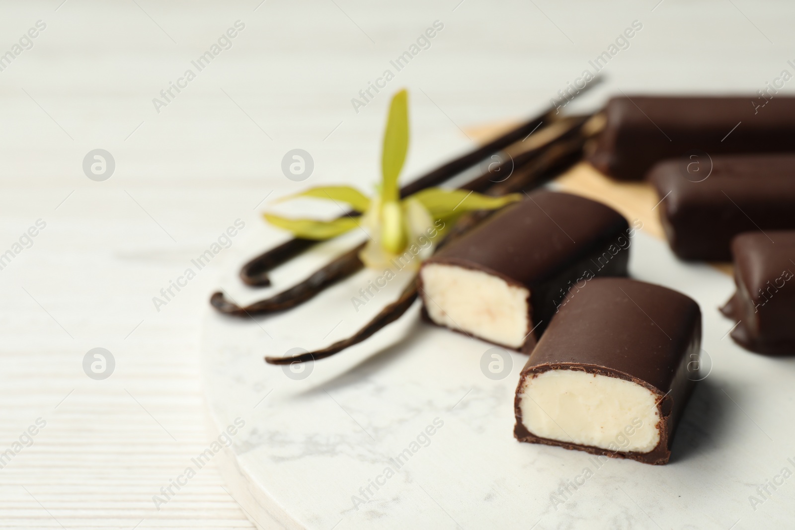 Photo of Glazed curd cheese bars, vanilla pods and flower on white table, closeup