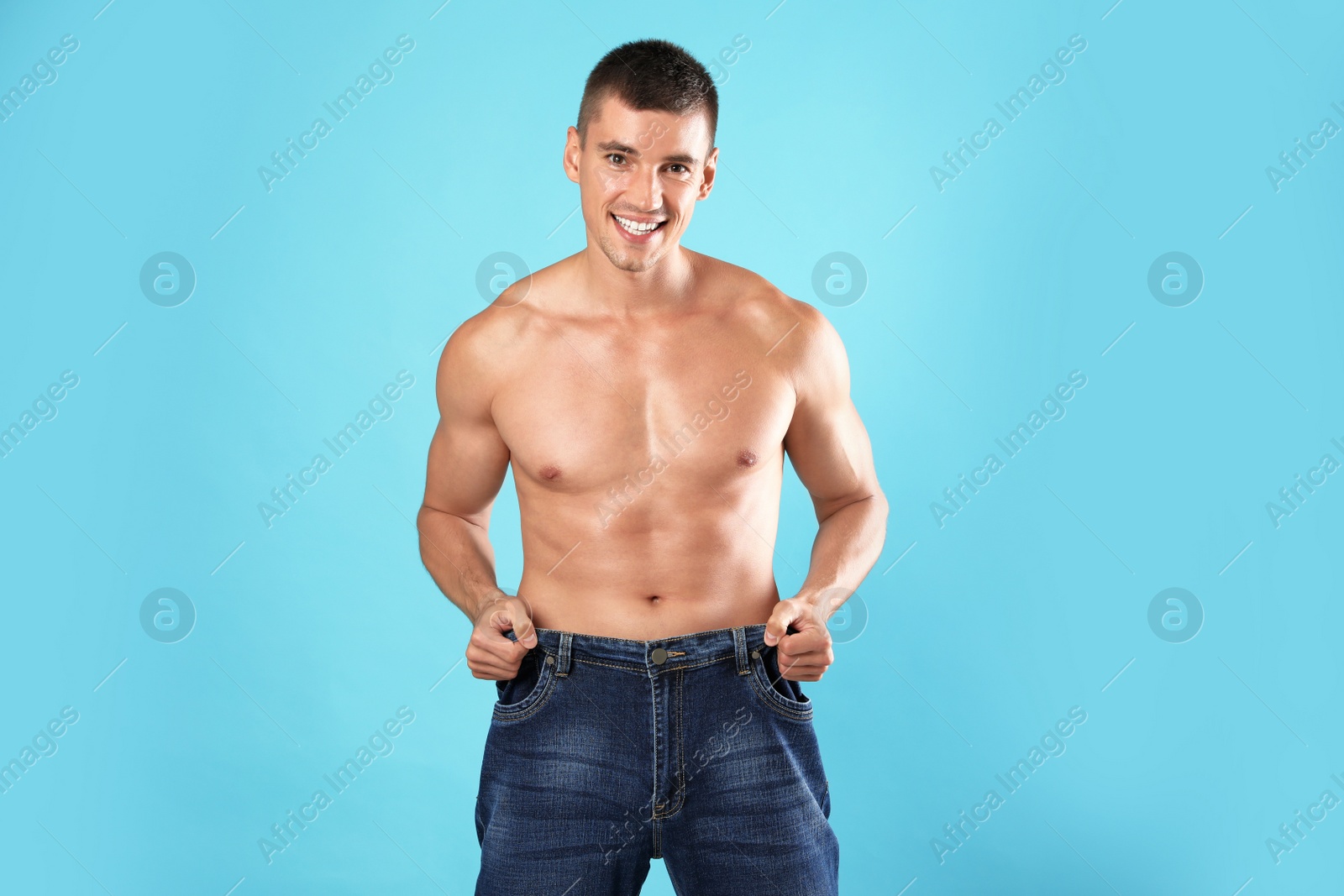 Photo of Young man with slim body in old big size jeans on light blue background