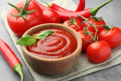 Photo of Bowl of tasty ketchup and ingredients on light grey table, closeup