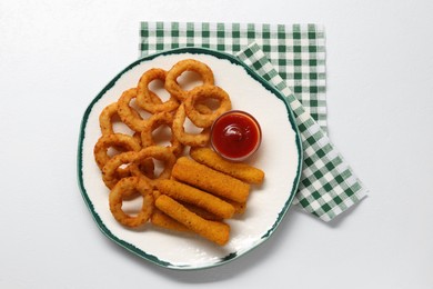 Plate with tasty ketchup, cheese sticks and onion rings on white table, top view