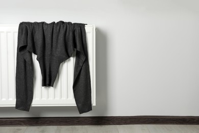Grey turtleneck sweater on heating radiator indoors. Space for text