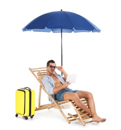 Photo of Young man with tablet and suitcase on sun lounger under umbrella against white background. Beach accessories