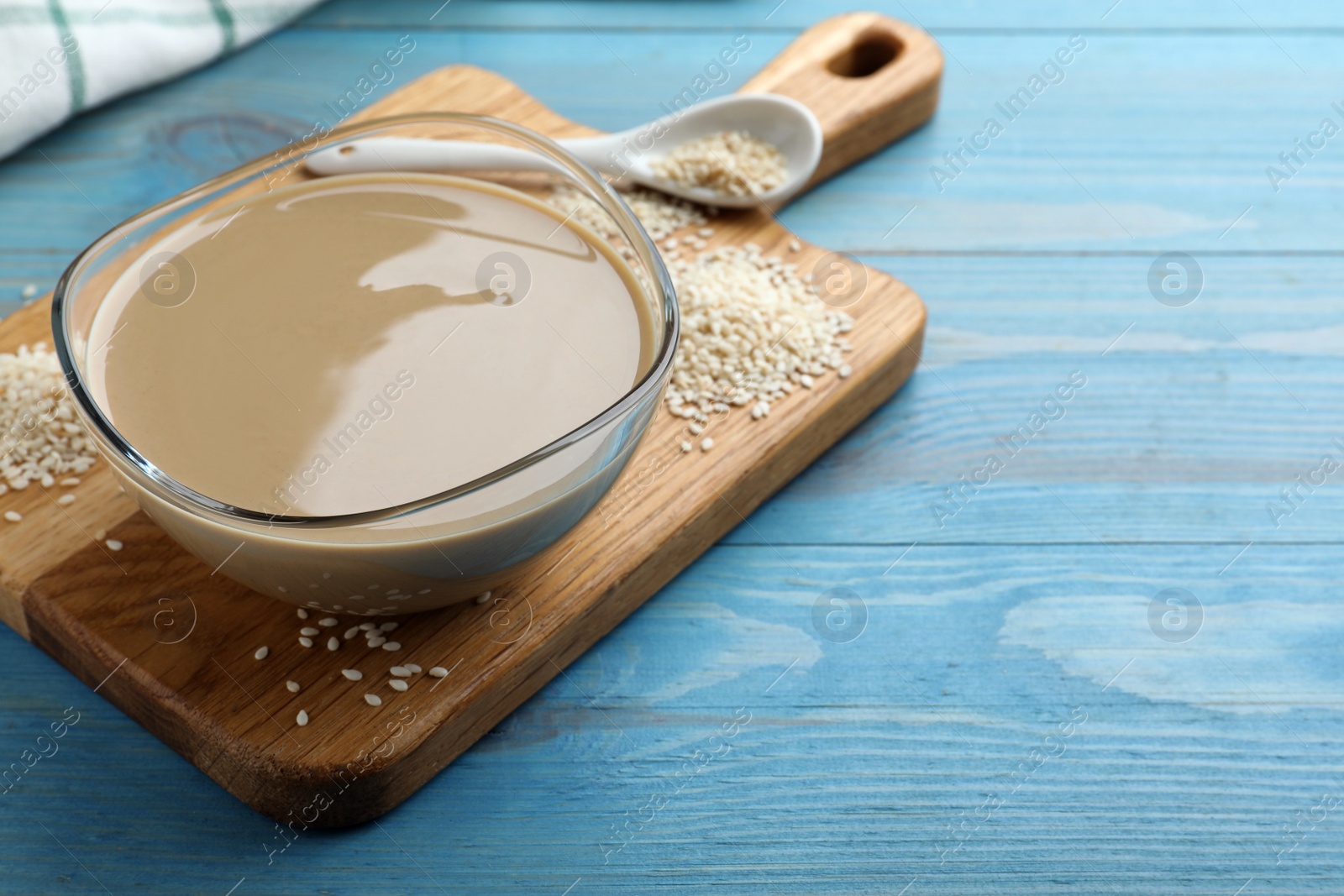 Photo of Tasty sesame paste and seeds on light blue wooden table, space for text