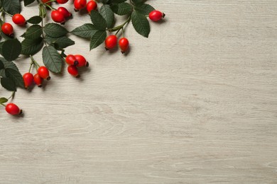 Photo of Ripe rose hip berries with green leaves on wooden table, flat lay. Space for text