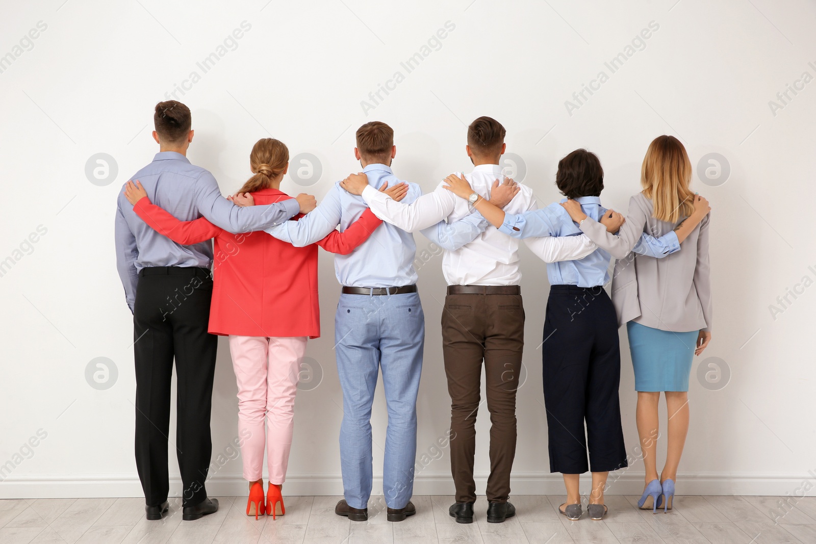 Photo of Group of young people hugging each other near light wall. Teamwork concept