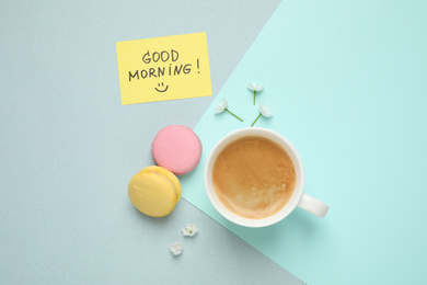 Photo of Delicious coffee, macarons, flowers and card with GOOD MORNING wish on color background, flat lay