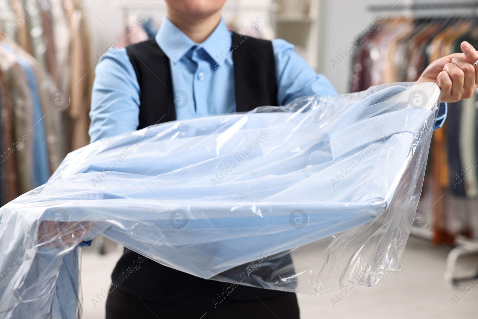 Photo of Dry-cleaning service. Woman holding shirt in plastic bag indoors, closeup