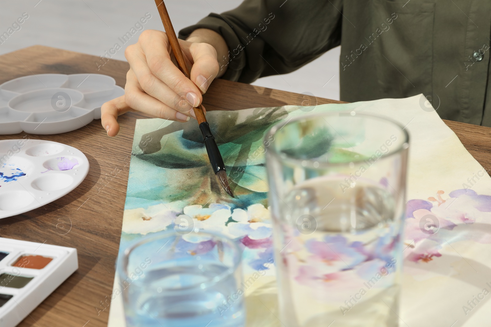 Photo of Woman painting flowers with watercolor at wooden table, closeup. Creative artwork