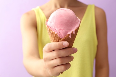 Photo of Woman holding pink ice cream in wafer cone on violet background, closeup