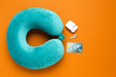 Photo of Turquoise travel pillow, credit card and earphones on orange background, flat lay. Space for text