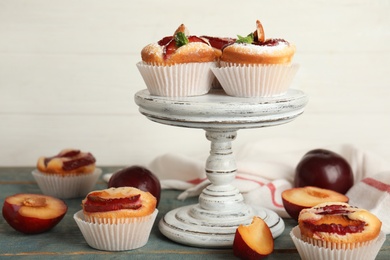 Photo of Delicious sweet cupcakes with plums on wooden table