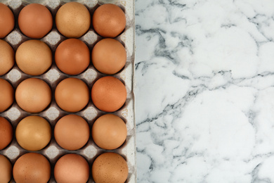 Photo of Raw chicken eggs on white marble table, top view. Space for text