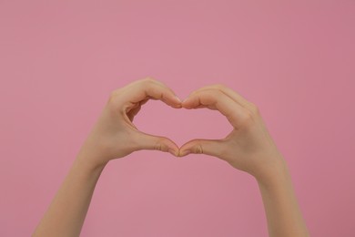 Photo of Woman making heart with fingers on pink background, closeup