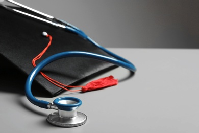Graduation hat and stethoscope on grey table, closeup view with space for text. Medical education