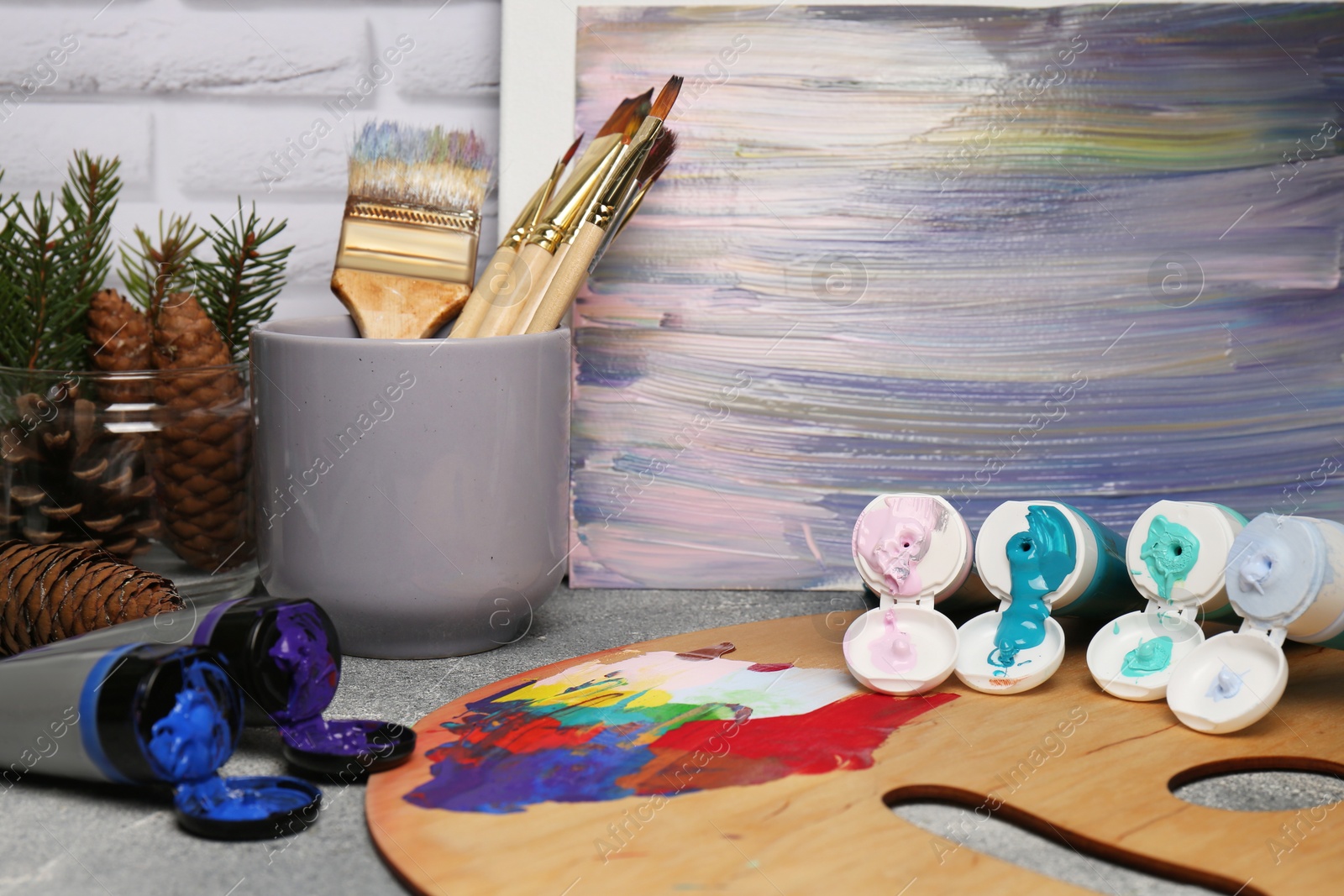 Photo of Artist's palette, tubes of colorful paint, brushes and canvas with abstract painting on textured table