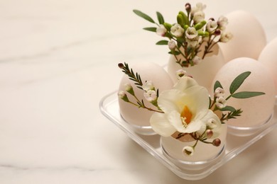 Photo of Easter eggs and beautiful flowers on white marble table, closeup. Space for text