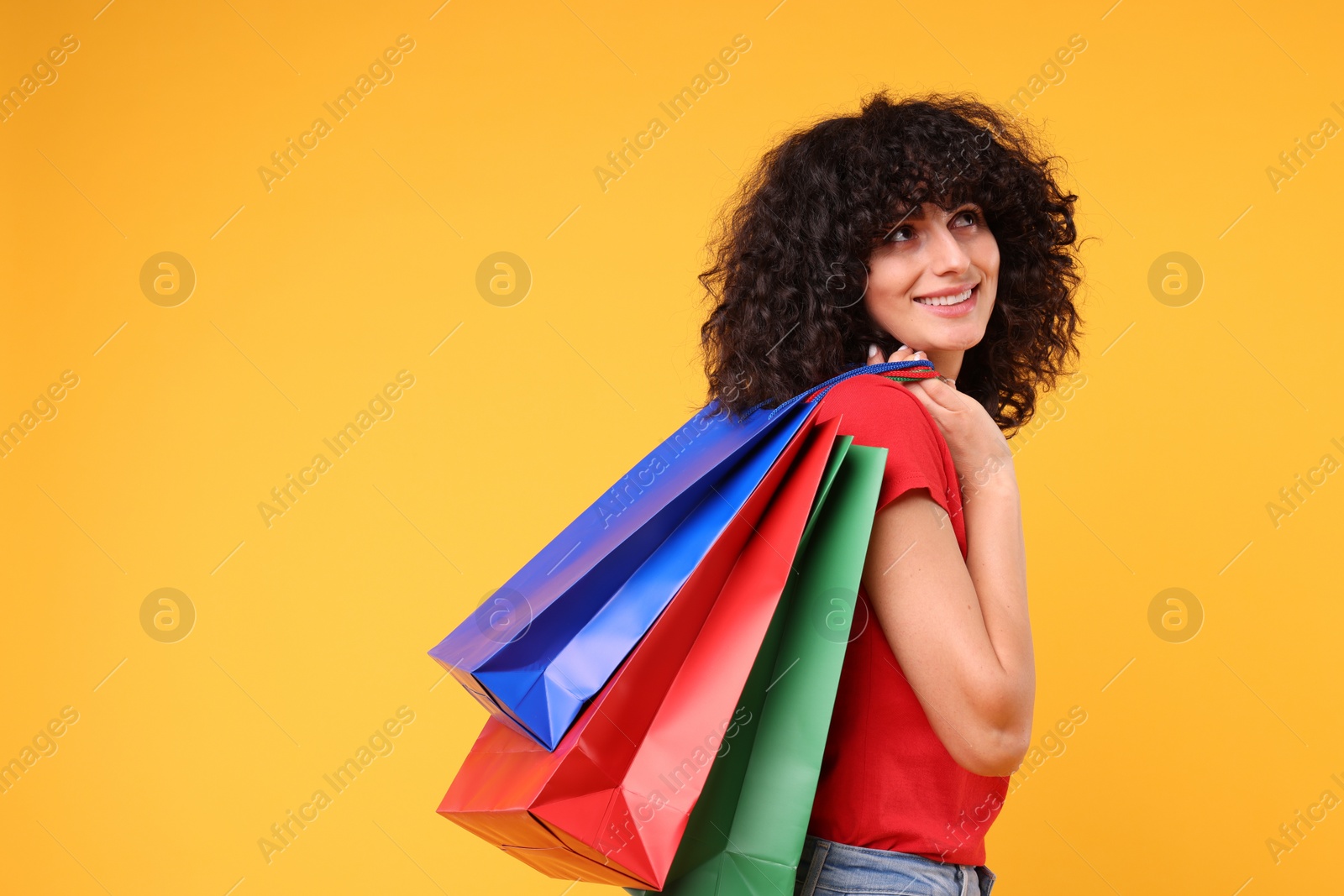 Photo of Happy young woman with shopping bags on yellow background. Space for text