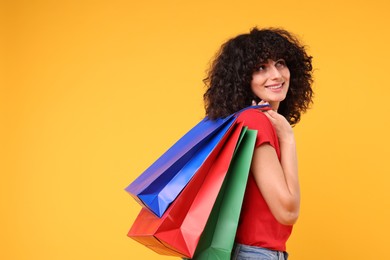 Happy young woman with shopping bags on yellow background. Space for text