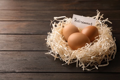 Photo of Eggs and card with word RETIREMENT in nest on wooden background, space for text. Pension concept