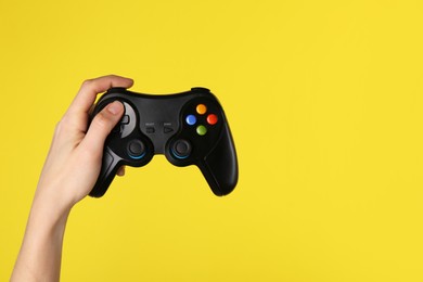 Photo of Woman using game controller on yellow background, closeup. Space for text
