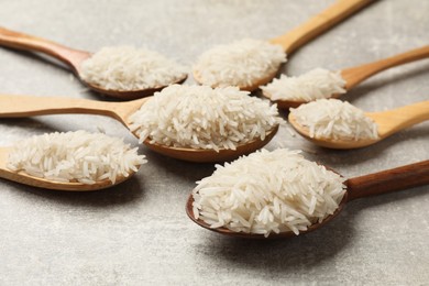 Photo of Raw basmati rice in spoons on grey table, closeup