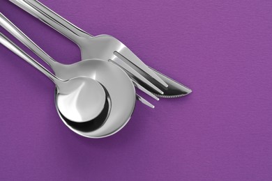 Photo of Fork, knife and spoons on purple background, flat lay with space for text. Stylish cutlery set