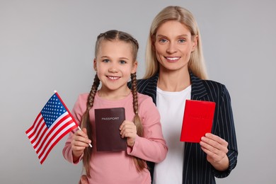 Immigration. Happy woman with her daughter holding passports and American flag on gray background