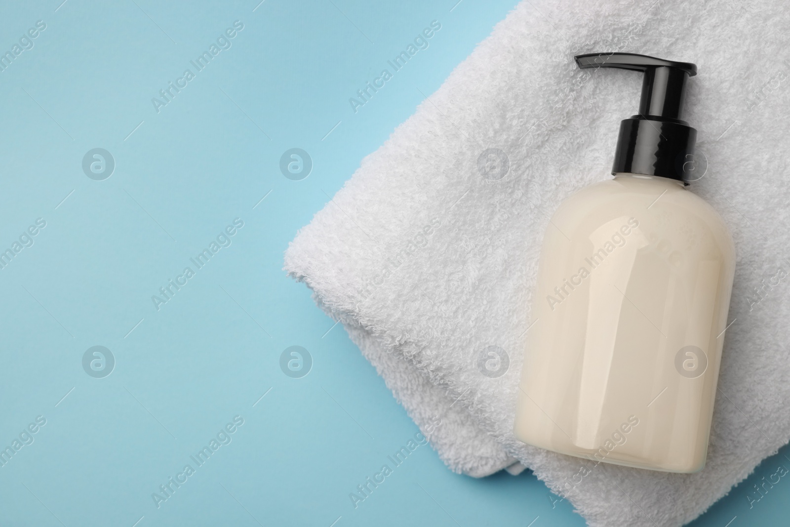 Photo of Bottle of liquid soap and towel on light blue background, top view. Space for text