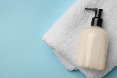 Photo of Bottle of liquid soap and towel on light blue background, top view. Space for text