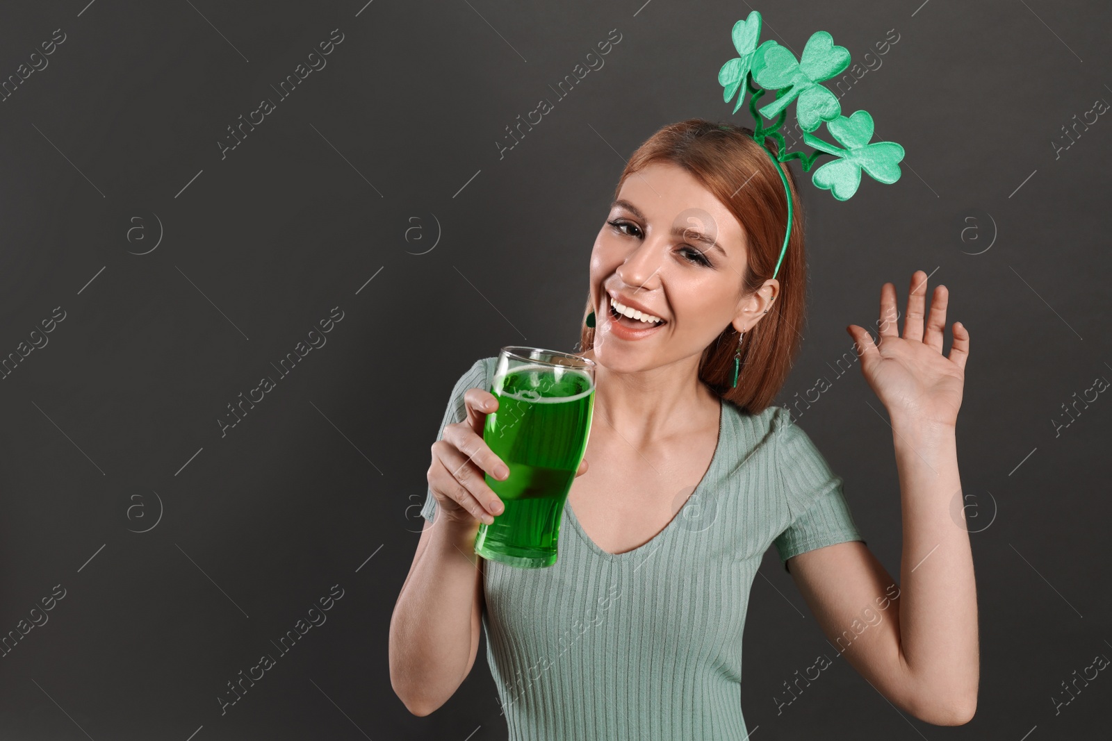 Photo of Young woman with clover headband and green beer on grey background, space for text. St. Patrick's Day celebration