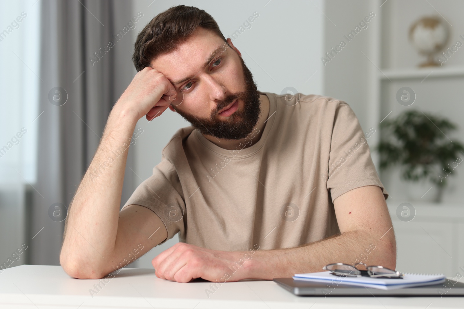 Photo of Overwhelmed man suffering from headache at table indoors