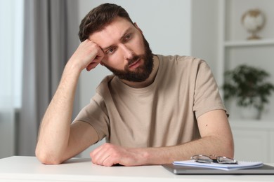 Photo of Overwhelmed man suffering from headache at table indoors